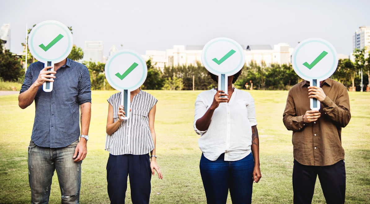 Four people holding green check signs on a field